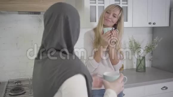 金发白种人女人听她的女性穆斯林朋友和拿着咖啡杯的肖像有朋友出去玩视频的预览图