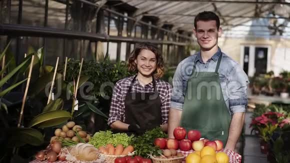 美丽的白种人农民肖像男人和女人在围裙出售有机食品在农场市场微笑着看着视频的预览图
