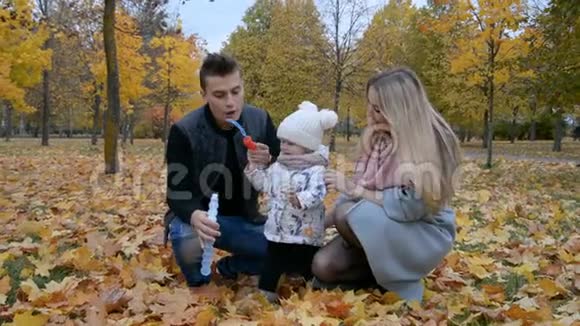 幸福的家庭观念爸爸妈妈和小女儿在秋天公园玩肥皂泡视频的预览图