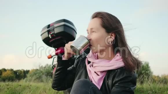 女摩托车旅行者在悬崖上度假时喝咖啡以摩托车为背景的游客在大自然中放松视频的预览图