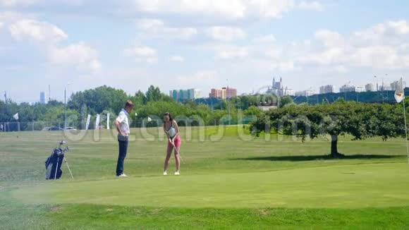 一个女孩在高尔夫球场上击球而一个男人正在观看视频的预览图