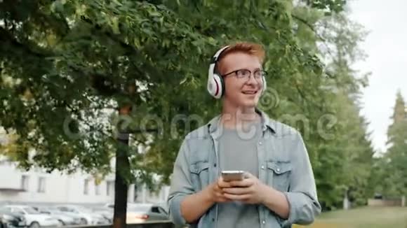 戴着耳机的快乐男人在公园里用智能手机听音乐视频的预览图