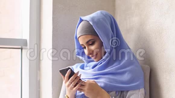 年轻的穆斯林女孩戴着头巾从智能手机发送信息视频的预览图
