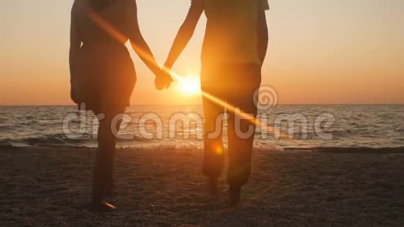 一对浪漫的年轻夫妇站在海滨的剪影男人走过来牵着女孩手一起享受阳光视频的预览图