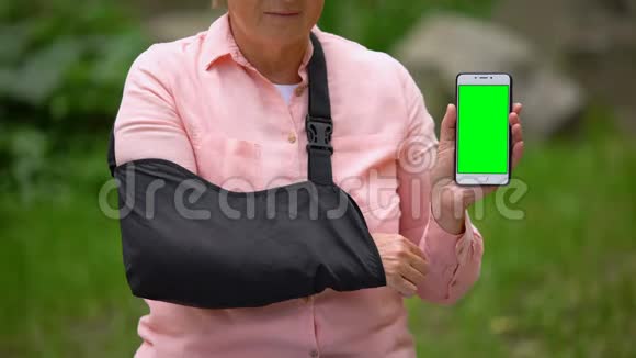 戴肩式固定吊带的高级女性显示智能手机绿色屏幕视频的预览图