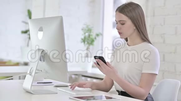 有魅力的年轻女性使用智能手机和桌面工作视频的预览图