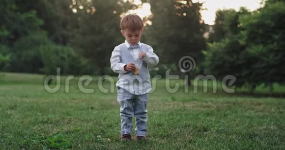 可爱的小男孩穿着休闲服在公园中央的镜头前吃着零食视频的预览图