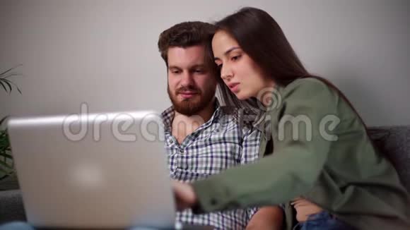 年轻幸福夫妇坐在柔软的沙发上用笔记本电脑的画像视频的预览图