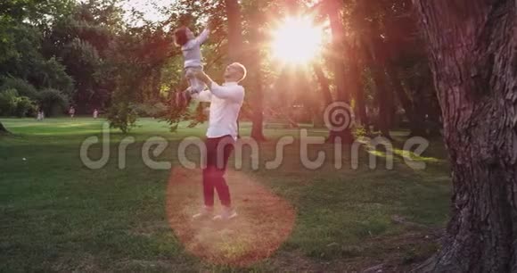 日落时分爸爸带着他的小男孩在公园里玩耍牵着儿子的手享受着时光他们穿着视频的预览图