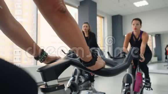 在健身俱乐部的自行车健身房妇女团体旋转自行车健身妇女骑自行车训练女运动员手视频的预览图