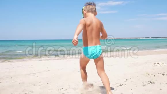 快乐的小男孩沿着海滩向大海跑去视频的预览图