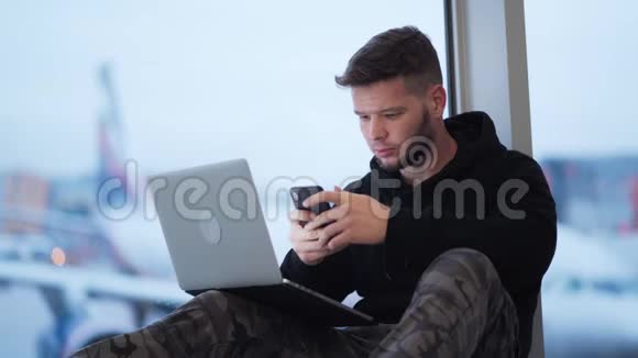 男子坐在机场使用智能手机和笔记本电脑飞机背景视频的预览图