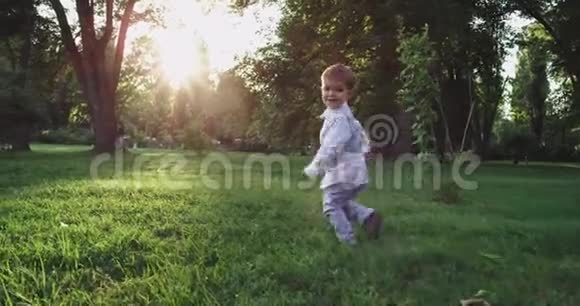 日落时分穿着一套可爱的西装在公园的草地上奔跑着一个滑稽的小男孩视频的预览图