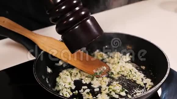 在炒洋葱大蒜和草药中厨师从胡椒瓶中加入胡椒粉视频的预览图