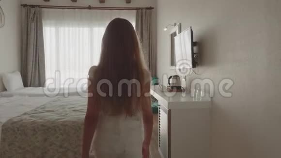 年轻女孩在白色设计的前卧室镜子里玩得很开心年轻女孩摇着白色的长发镜子视频的预览图