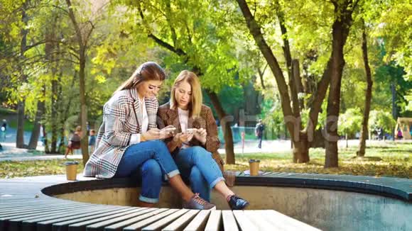 穿着时髦服装的快乐女孩在阳光明媚的花园里使用智能手机视频的预览图