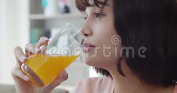 年轻漂亮的女人一边看电视一边喝橙汁视频的预览图