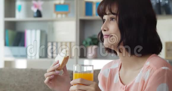 年轻漂亮的女人吃三明治和橙汁视频的预览图