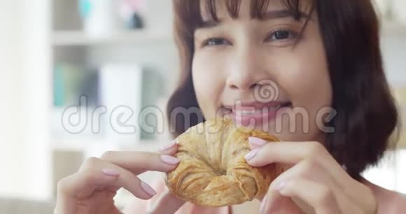 年轻的女人咬着吃一个大牛角面包和美味视频的预览图