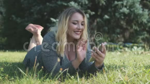 少女看手机躺在自然草坪上视频的预览图