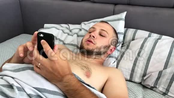 一个年轻人躺在床上在智能手机上写着东西俯视图视频的预览图