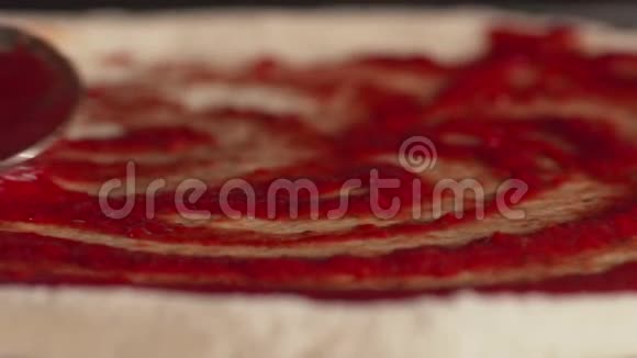 勺子抹上面团上的酱汁在披萨面团上用勺子涂抹番茄酱视频的预览图
