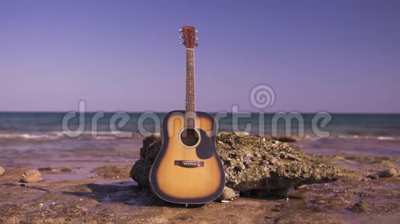 在海滩或海岸或海洋上的西方吉他吉他独自靠岸海浪在石头上岩石上视频的预览图