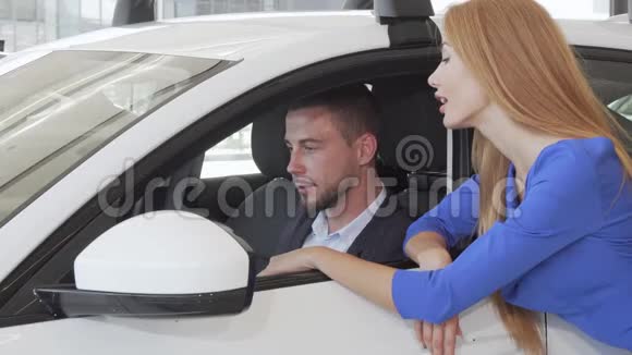 英俊的男人在经销商沙龙挑选新车时与妻子交谈视频的预览图