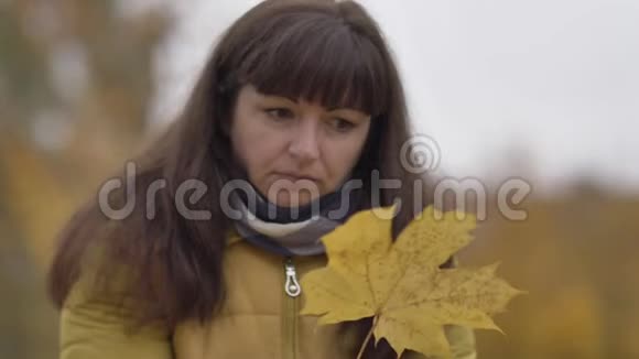 伤心的女人手里拿着枫叶在秋天的户外慢动作中想着什么视频的预览图