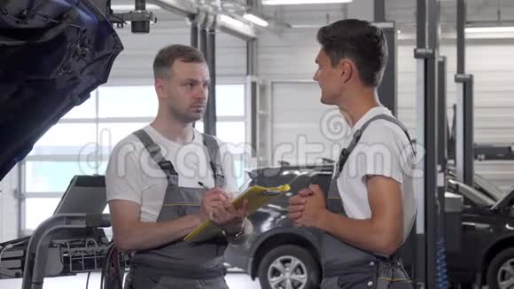 年轻的男汽车修理工在车库和他的同事交谈视频的预览图