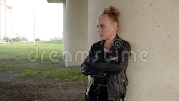 穿着黑色皮夹克的胖女孩站在桥下在工业景观上摆着摄像机的摇滚女孩视频的预览图