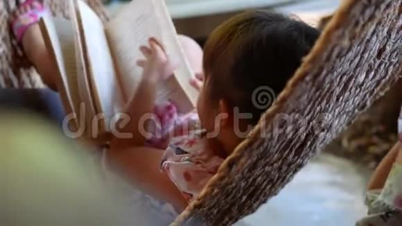 可爱的小女孩放松和阅读一本书躺在吊床户外花园视频的预览图