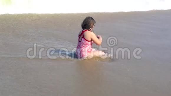 小女孩坐在海边的沙滩上海浪在她的身体里飞溅视频的预览图