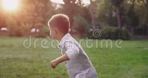 可爱的男孩穿着休闲时尚的西装跑过公园非常精力充沛微笑着大看着他的相机视频的预览图