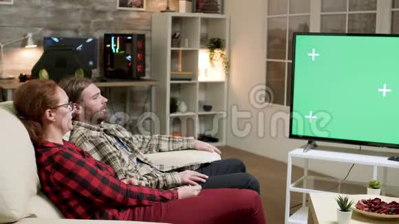hipster夫妇坐在电视机前的沙发上屏幕是绿色的视频的预览图