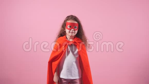 漂亮的小卷发女孩穿着红色英雄套装戴着粉红色背景的面具视频的预览图