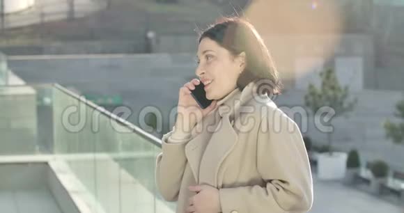 微笑的白人妇女站在阳光下打电话的侧视图漂亮的黑发女商人视频的预览图