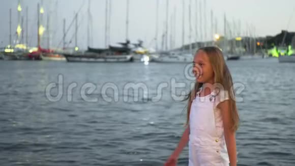 在傍晚的海港风景中一个在风中挥动头发的少女在海上和游艇背景下许愿的快乐女孩视频的预览图