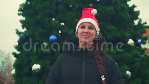 一幅快乐英俊的女人的肖像戴着圣诞老人的帽子穿着一件黑色夹克自信地看着相机微笑着视频的预览图