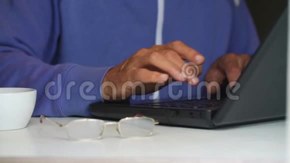老人在笔记本电脑上打字杯子和桌子上的眼镜视频的预览图