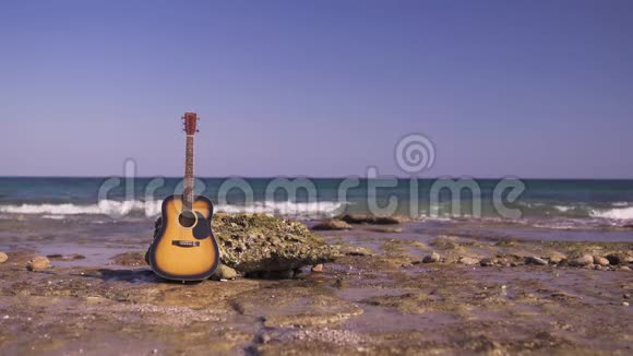 在海滩或海岸有背景海或海洋的声学西方吉他只有一把吉他在大海上石头上有波浪视频的预览图