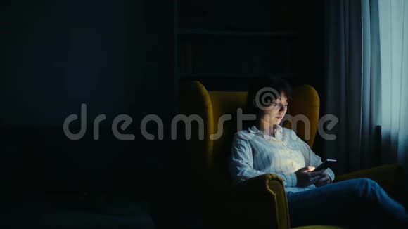 穿着休闲服装微笑的年轻女人在黑暗的房间里用电话视频的预览图