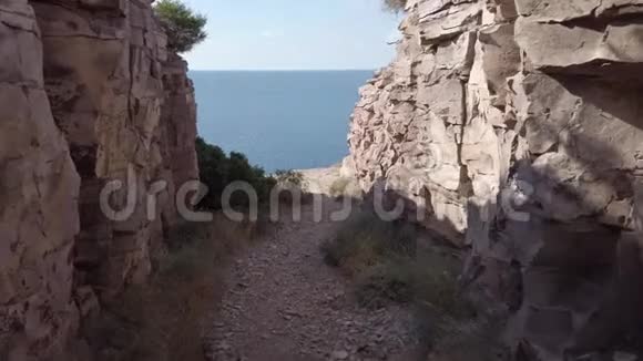 探索由岩石墙包裹的岩石小径直到蓝色的大海中的悬崖视频的预览图