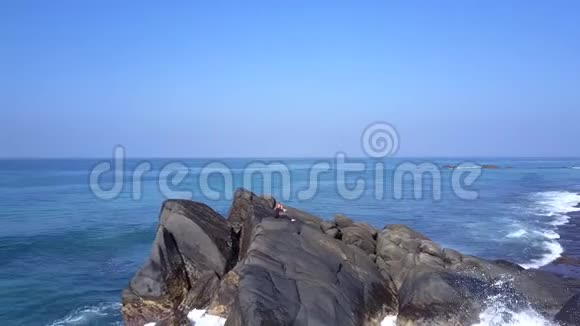 女孩坐在被海水冲刷的岩石峭壁上做瑜伽姿势视频的预览图