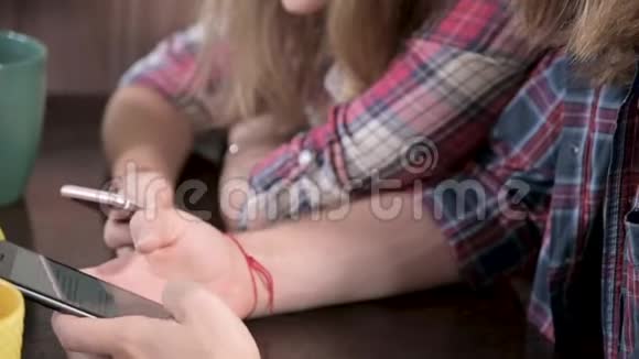 一对留着长发的年轻的梅勒妮正坐在餐桌旁手里拿着电话冲浪视频的预览图