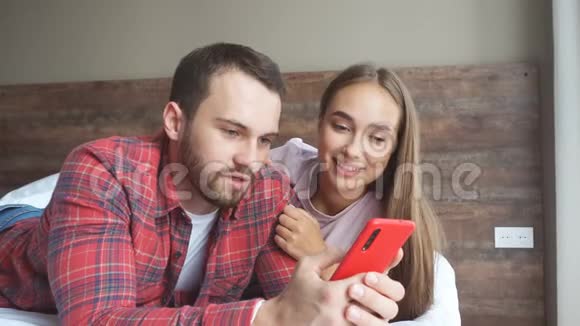 一对幸福的情侣拿着红色小玩意用手机看有趣的视频视频的预览图