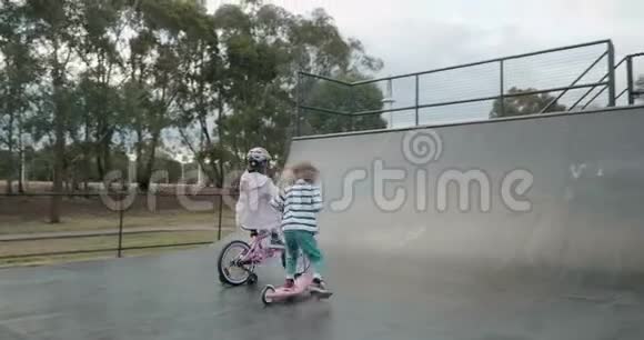 一个小男孩在滑板车上溜冰女孩骑自行车在滑板坡道上半管视频的预览图