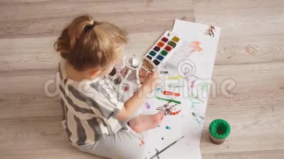 小可爱的孩子在坐在地板上的客厅里的纸上画着五颜六色的颜料视频的预览图