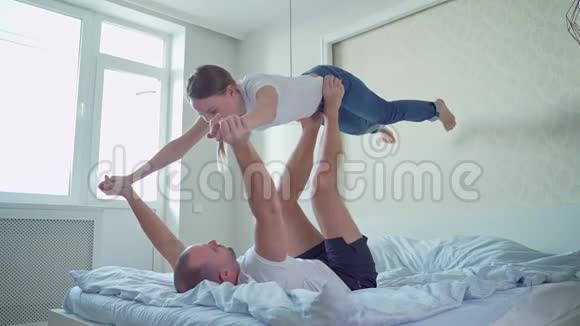 快乐的一对夫妇在床上玩玩得很开心男人躺在床上用双脚握住妻子的手举起妻子视频的预览图