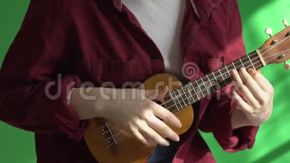 在绿色背景下年轻的时髦女人弹着四弦琴吉他4K视频的预览图